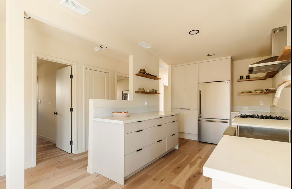 Minimalist white kitchen with a drawer island and open wood shelving.